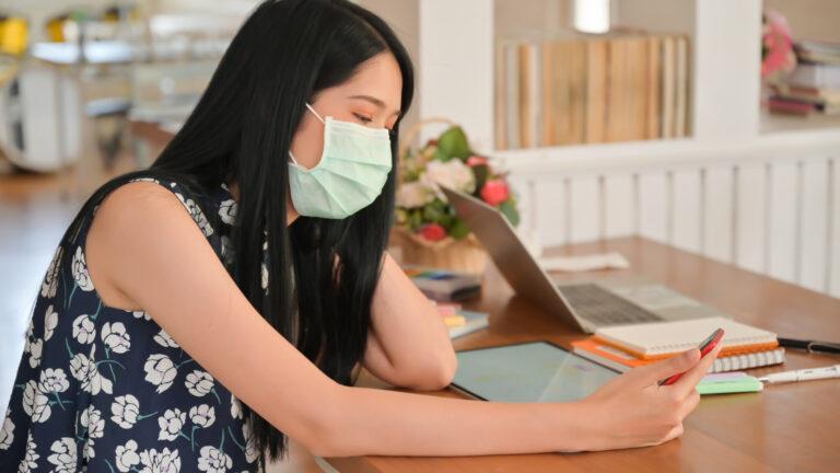Woman wearing a mask is using a smartphone in a cafe.She is at r